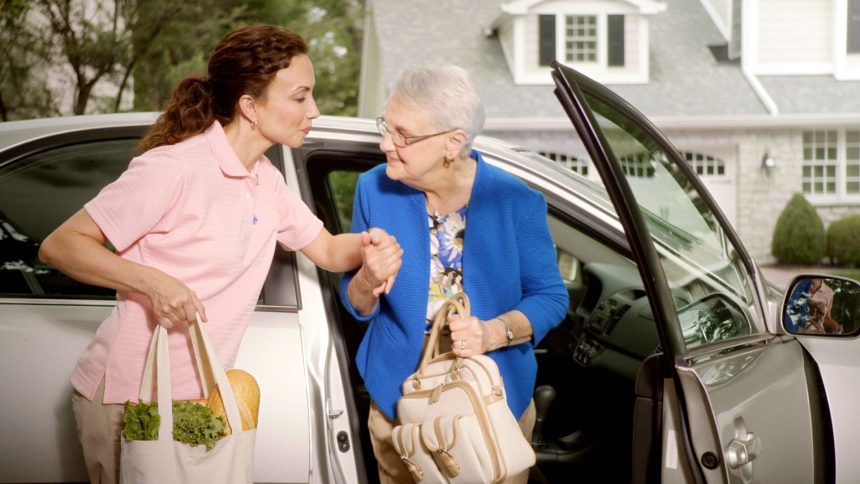 A younger woman assisting an elderly woman out of a car.